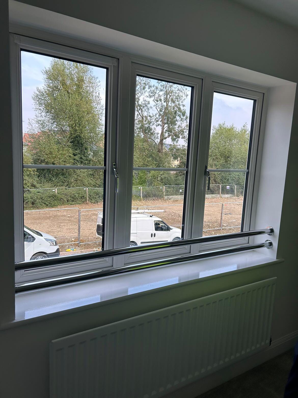 An image of a window taken from inside a new build house. The windows open outwards but are guarded by two horizontal metal poles inside the house, covering the lower end of the window.