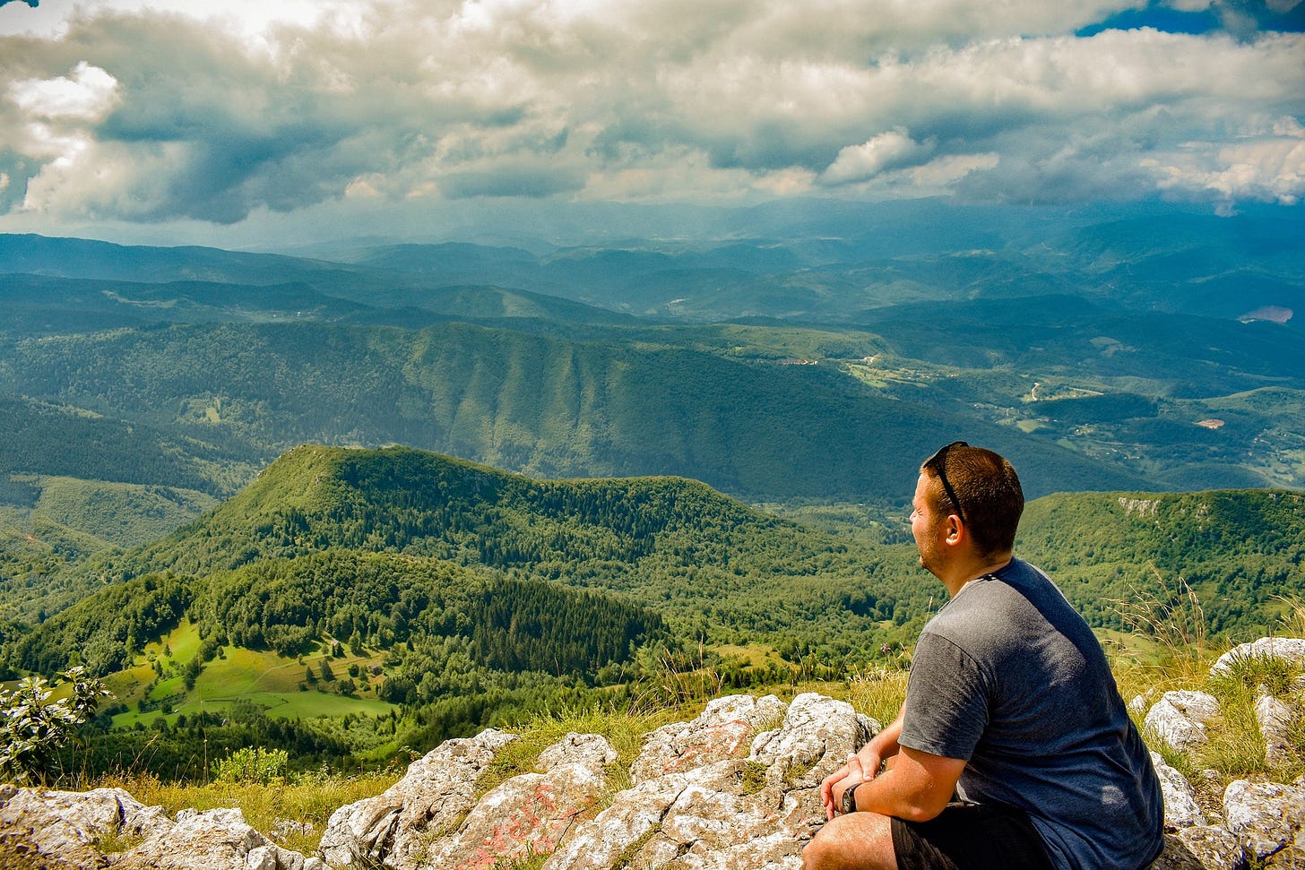 A man sits and looks over a vista of hills.