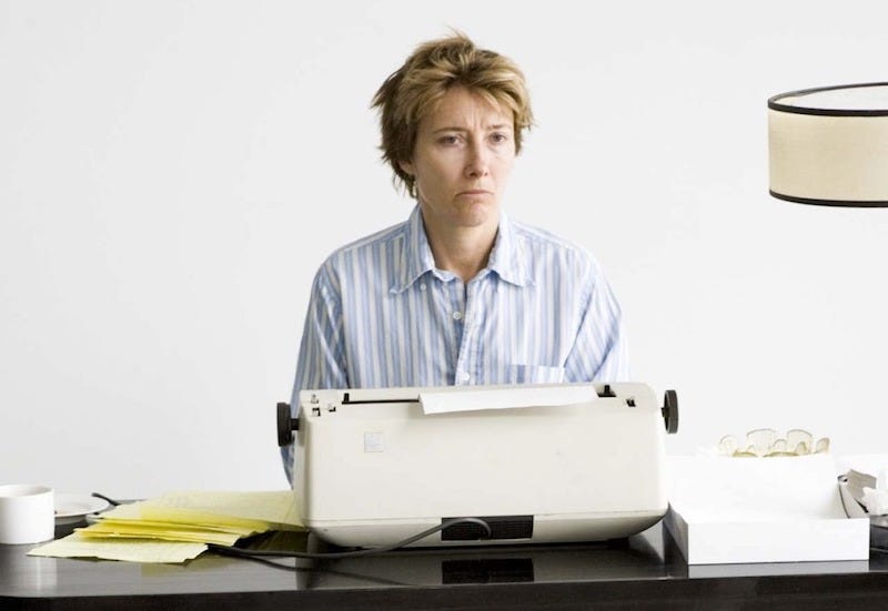 Emma Thompson as Karen Eiffel in Stranger Than Fiction (2006), sitting at a typewriter in pyjamas looking miserable