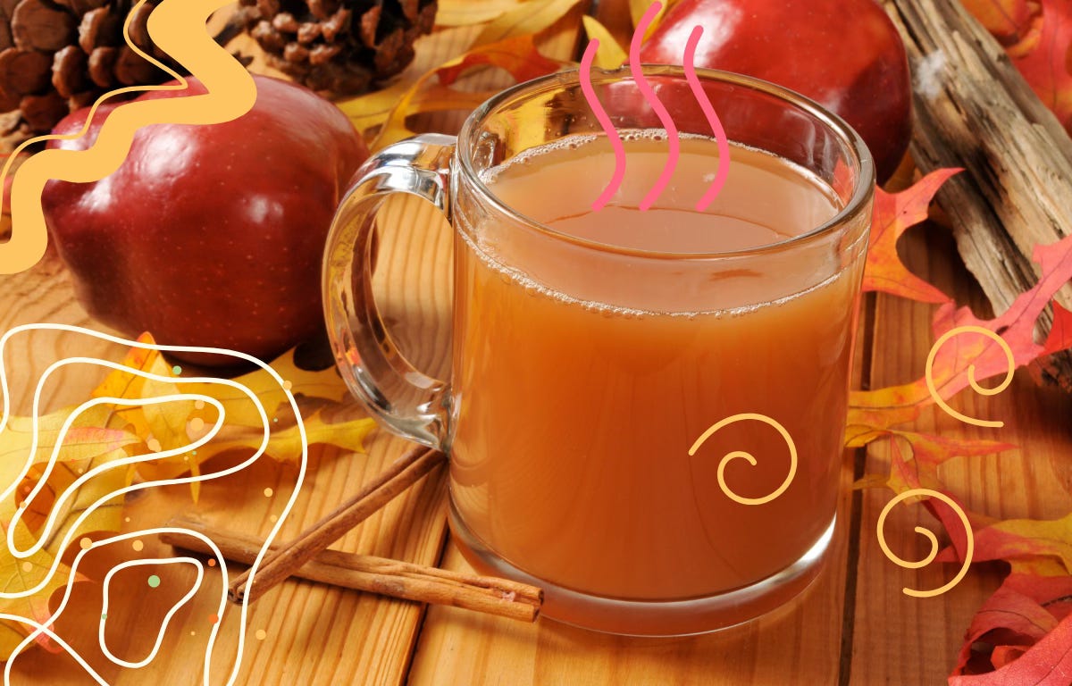 A mug of warm mulled cider with cinnamon sticks, apples and pinecones on a table