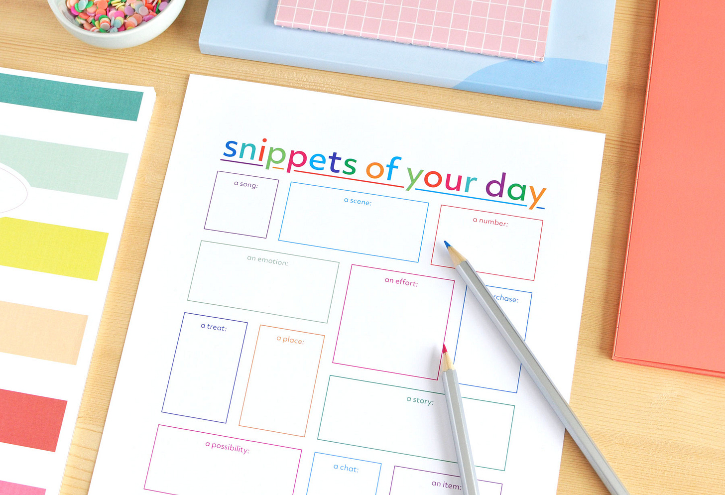 Features a colourful printable journal page entitled "Snippets of your day", on a wood surface with colourful pencils and notebooks.