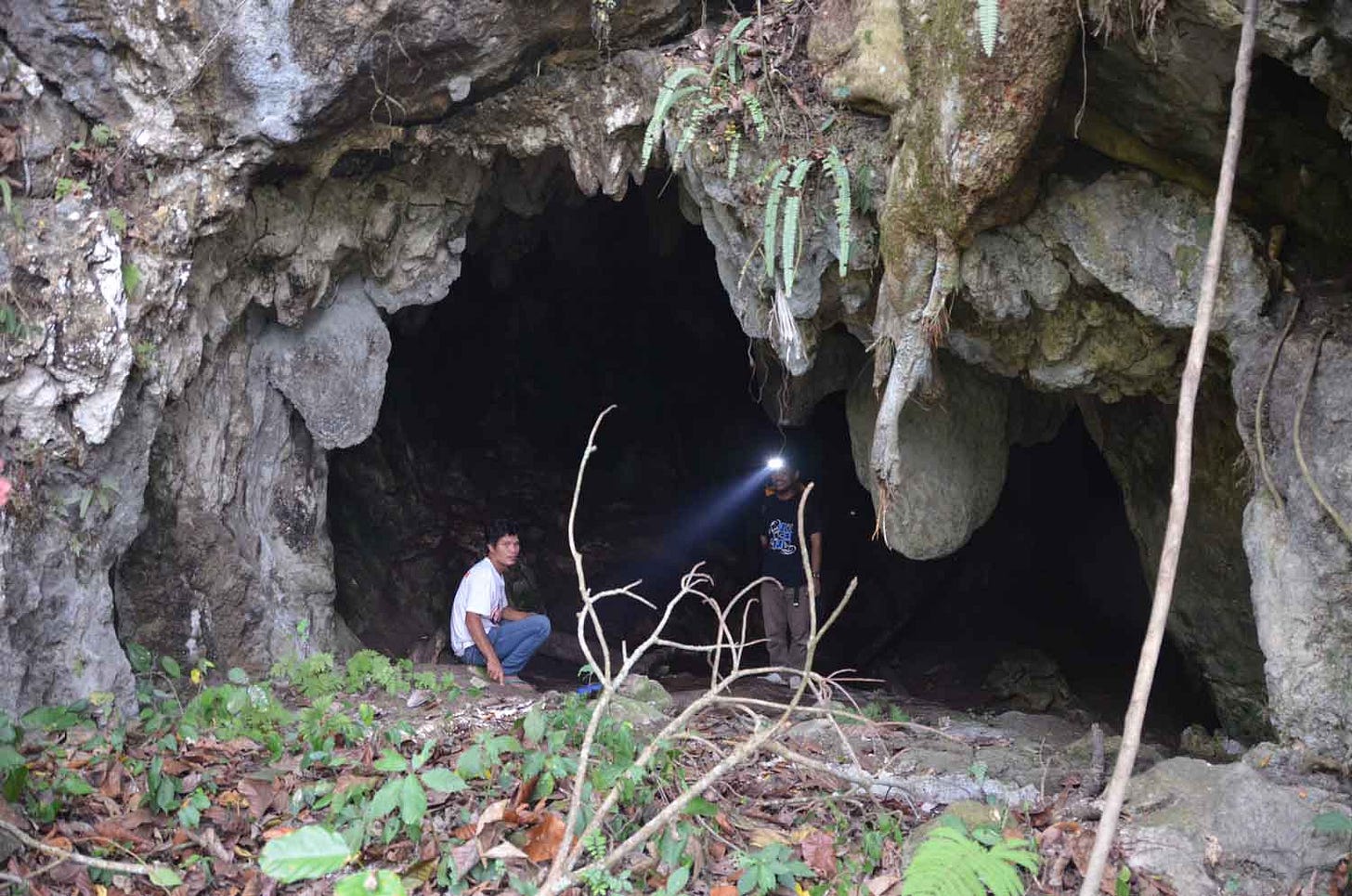 A cave entrance with two people, one with headlight A cave entrance with two people, one with headlight