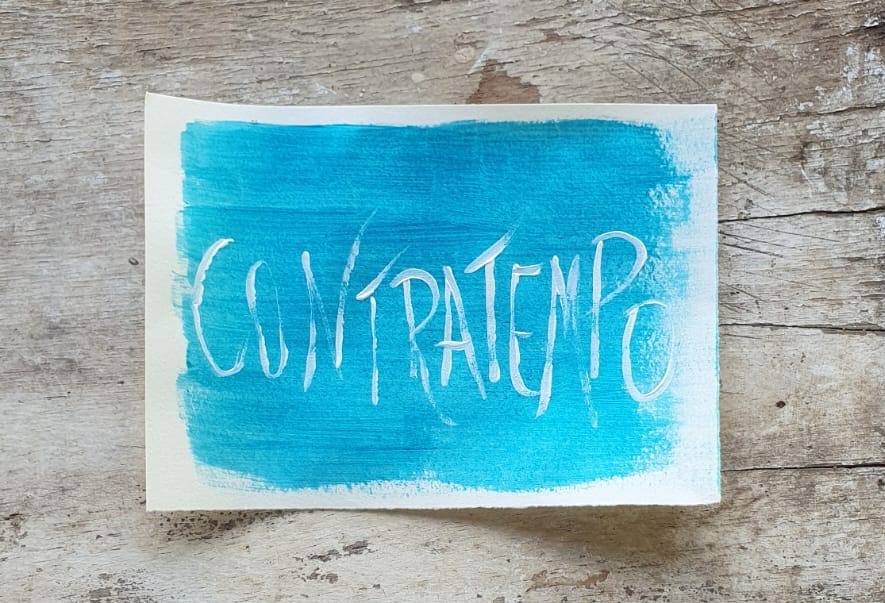 Fotografia de um papel pintado de azul claro, com a palavra Contratempo escrita, sobre um fundo de madeira 