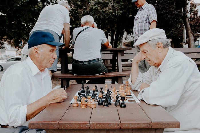 two older men playing chess in a park somewhere. One day I will join them, but first I need people to subscribe to my Substack https://smillew.substack.com/