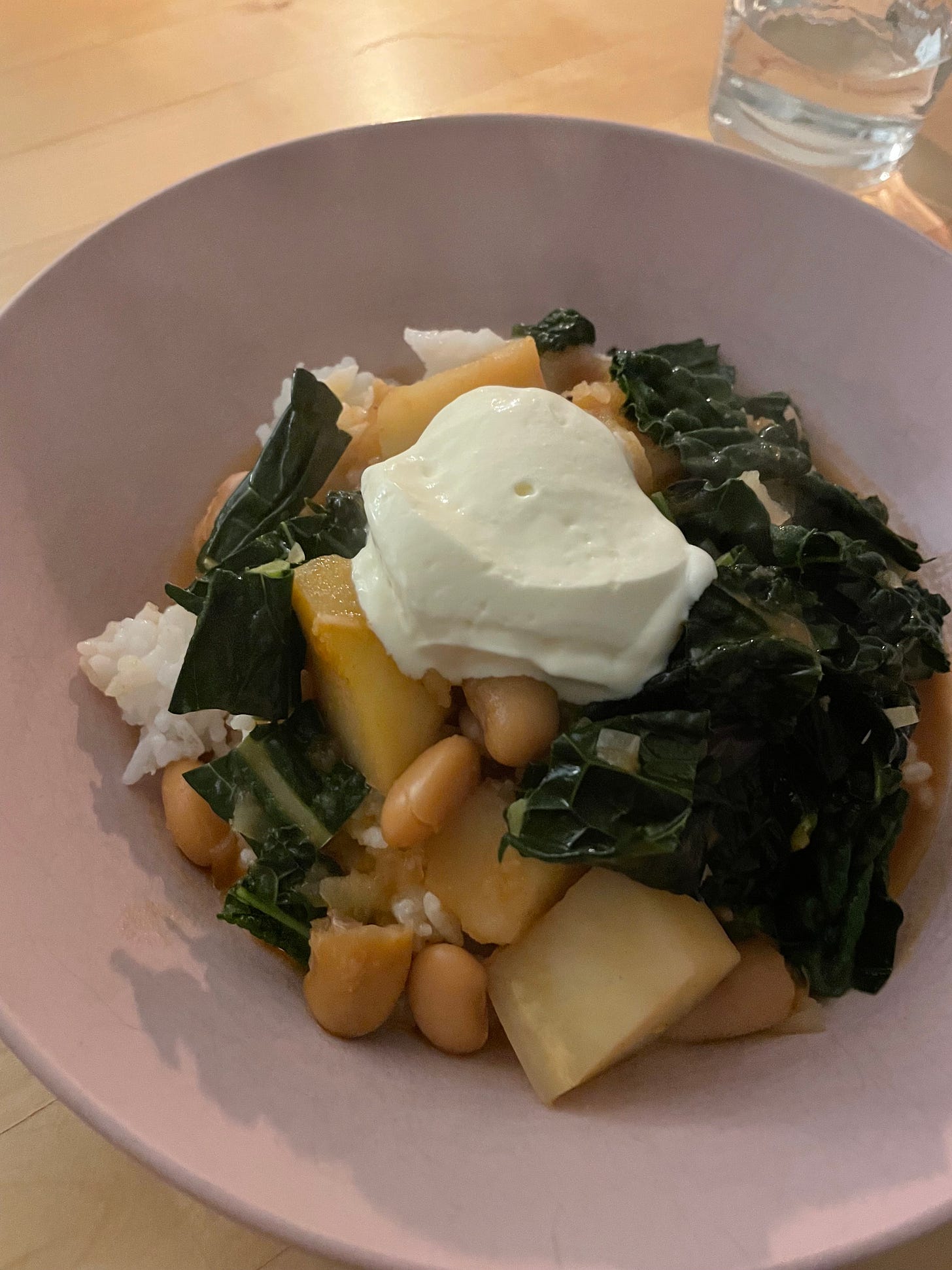 Pink bowl filled with white rice and topped with gochujang potato stew, made with butter beans and greens. Served with a blob of sour cream.
