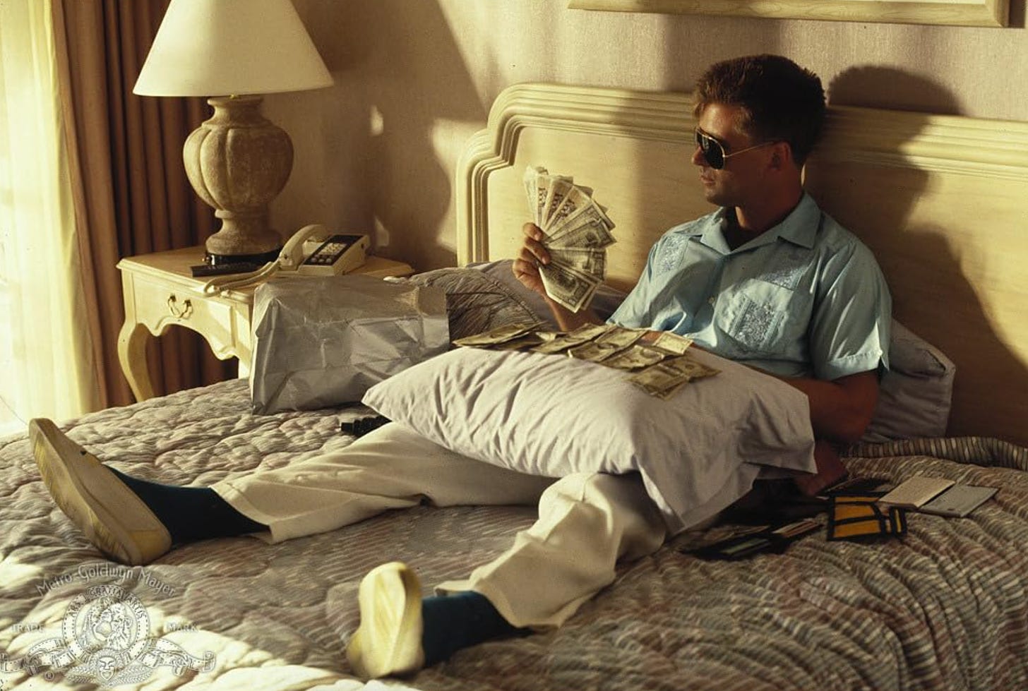 Alec Baldwin sitting on a hotel bed with his shoes on and counting big bills in "Miami Blues" (1990)