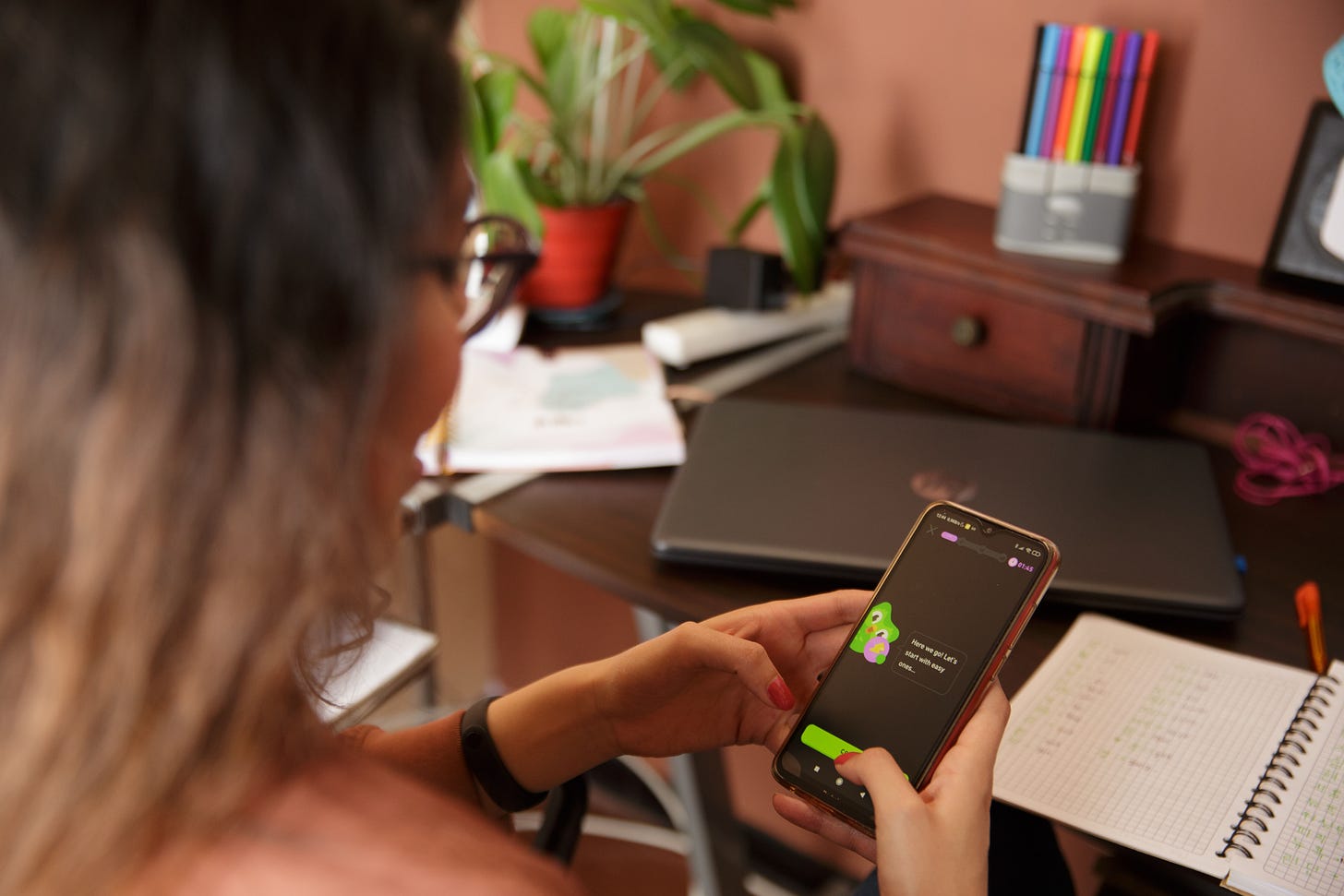 A woman holding a smartphone with the Duolingo app open