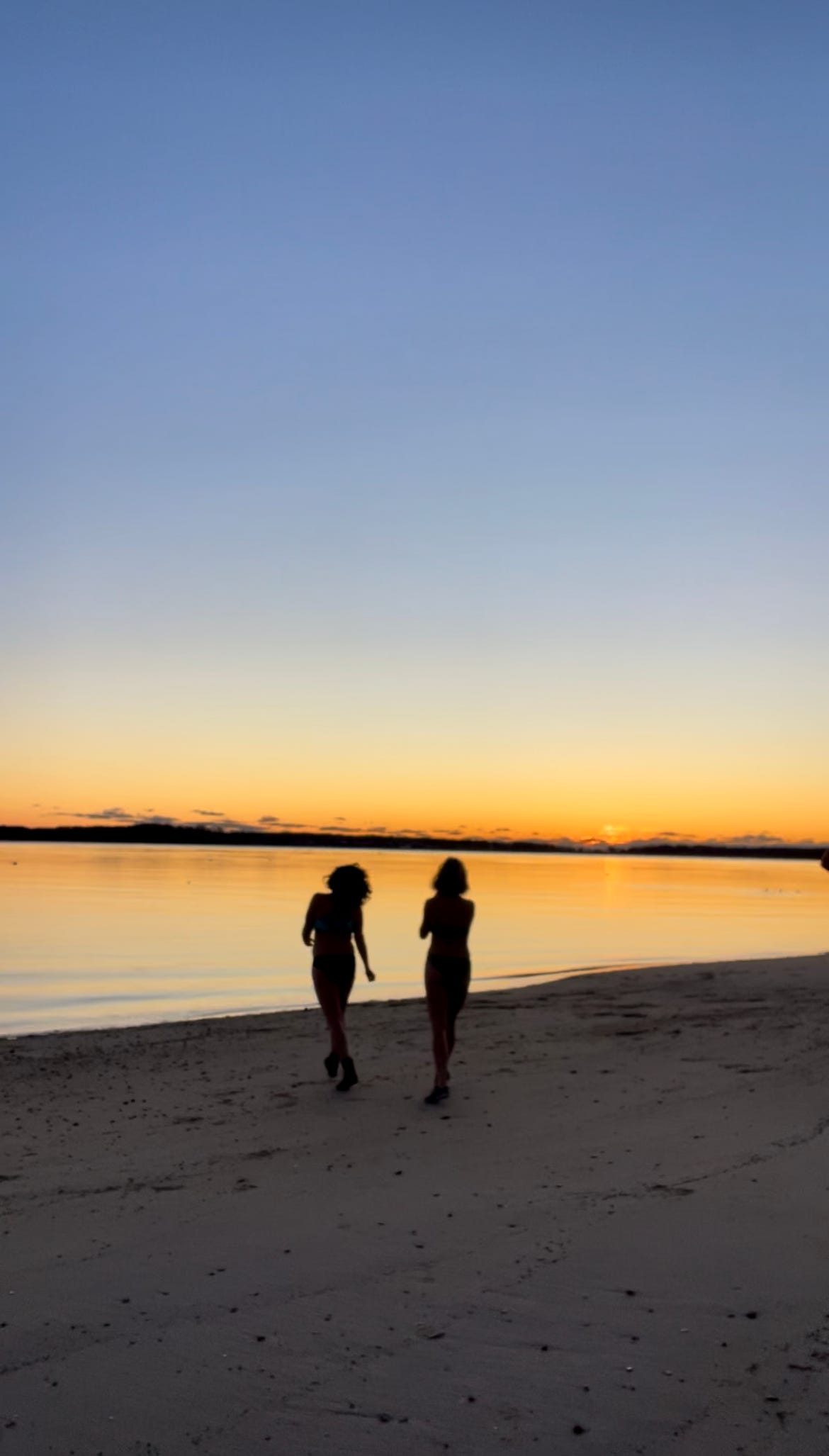 Two women silhouetted in the dawn against the ocean