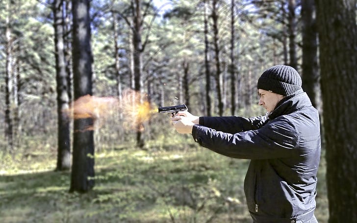 man firing semi-automatic rifle in a forest during daytime