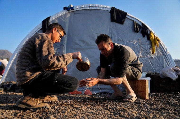 A boy helps his father wash his hands at a makeshift camp in Iskenderun, southern Turkey (Photo: Hussein Malla/AP)