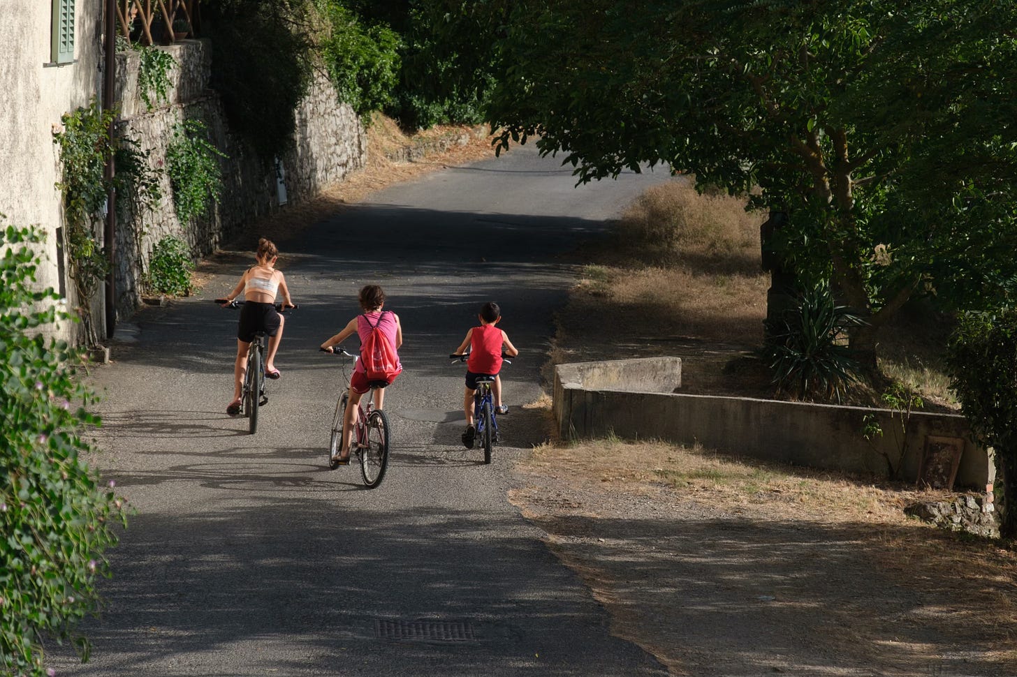 Three children riding bicycles on a rustic road 
