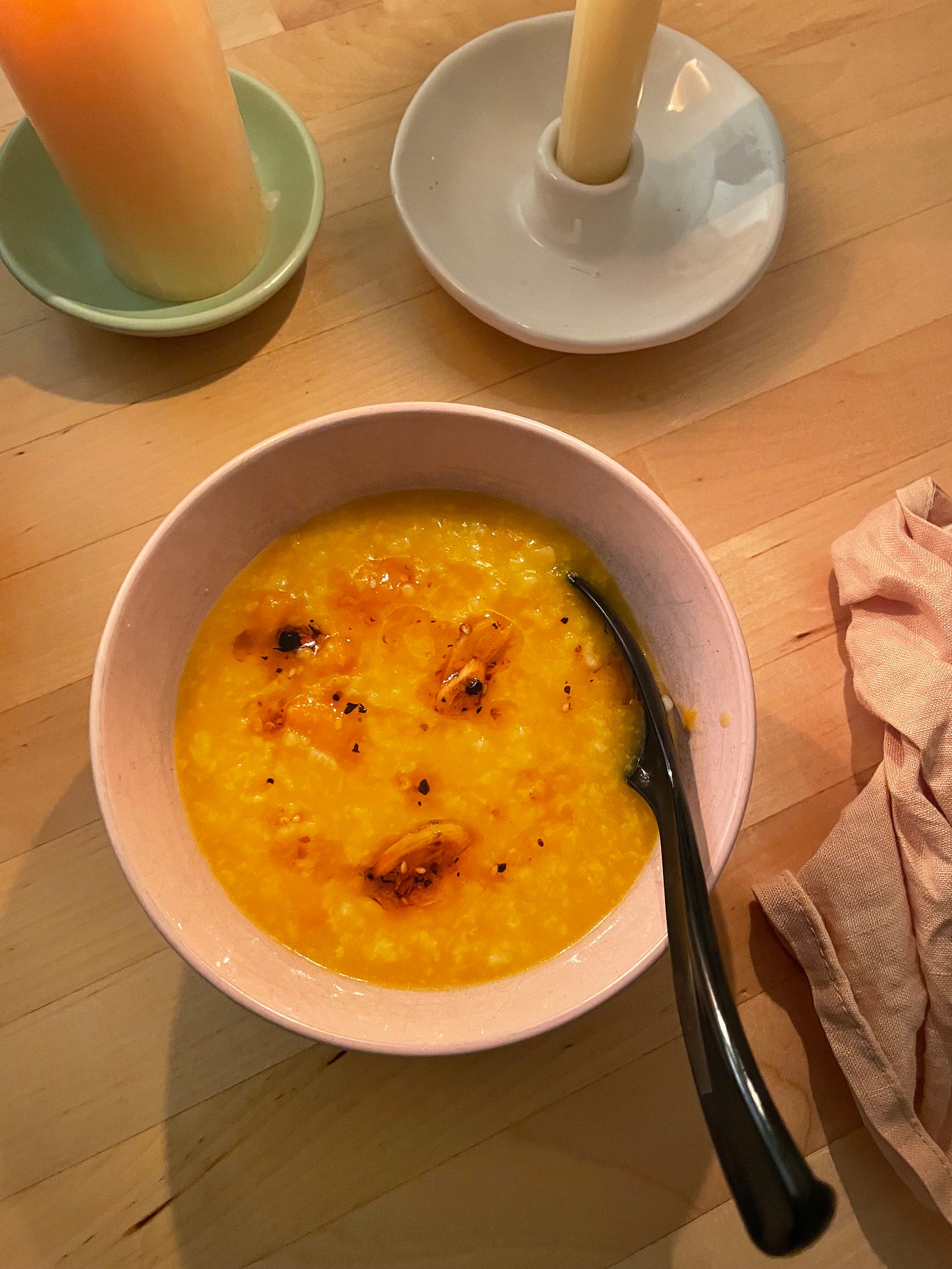 Bowl of pumpkin congee which is orange in colour, chilli oil swirled on top.