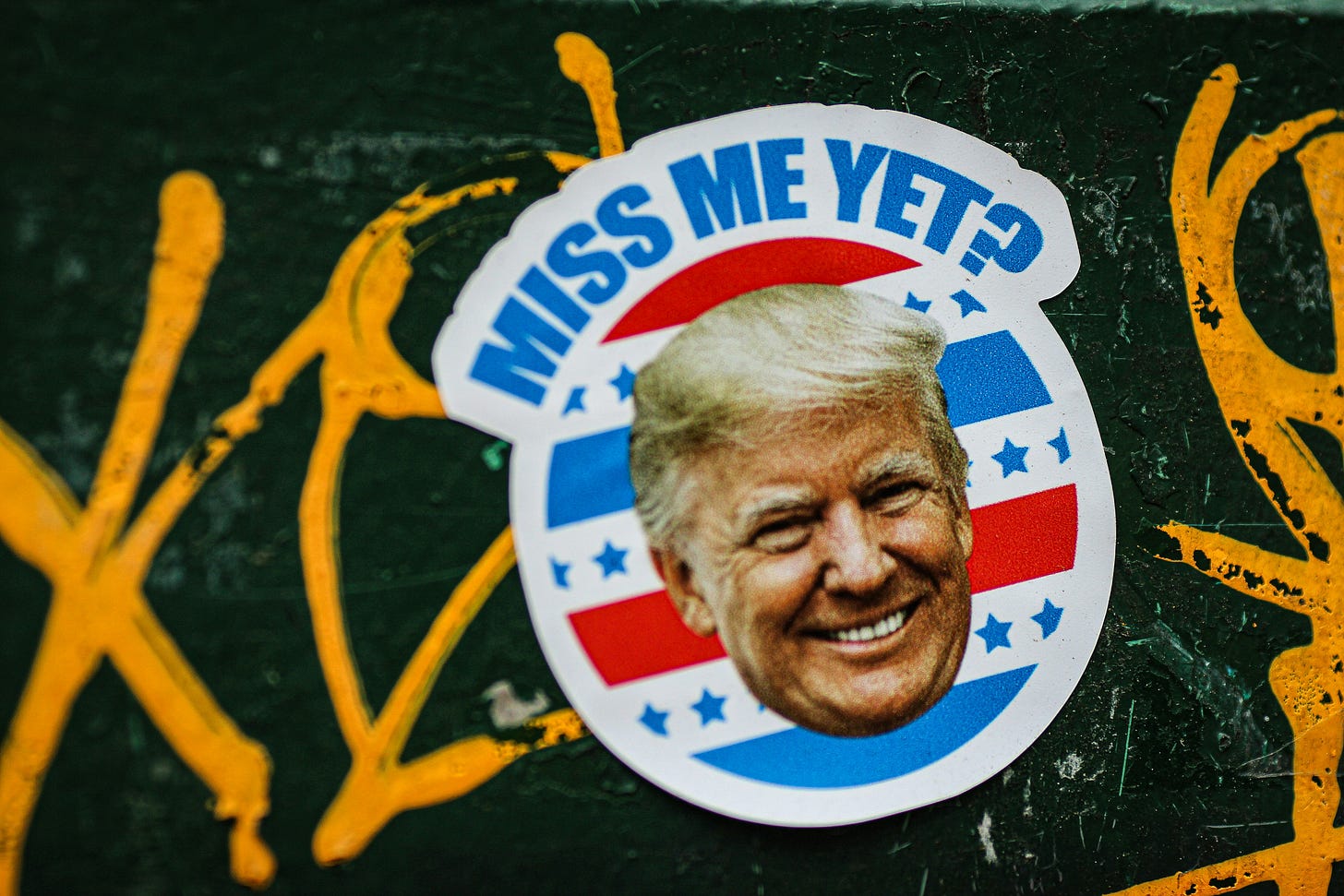 A sticker with Donald Trump's face that reads "Miss me yet?" on a wall.