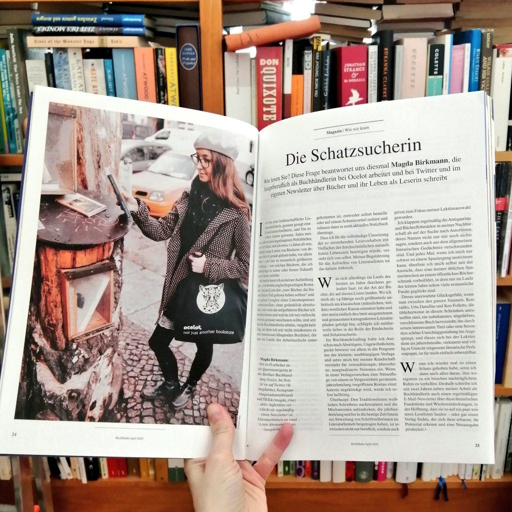 Meine Hand hält das Magazin so geöffnet, dass man eine Doppelseite sieht, links ist ein ganzseitiges Farbfoto von mir zu sehen, wie ich neben einem öffentlichen Bücherschrank stehe und auf ein Buch in meiner Hand gucke. Auf der rechten Seite steht ein ganzseitiges Text von mir mit der Überschrift "Die Schatzsucherin" 