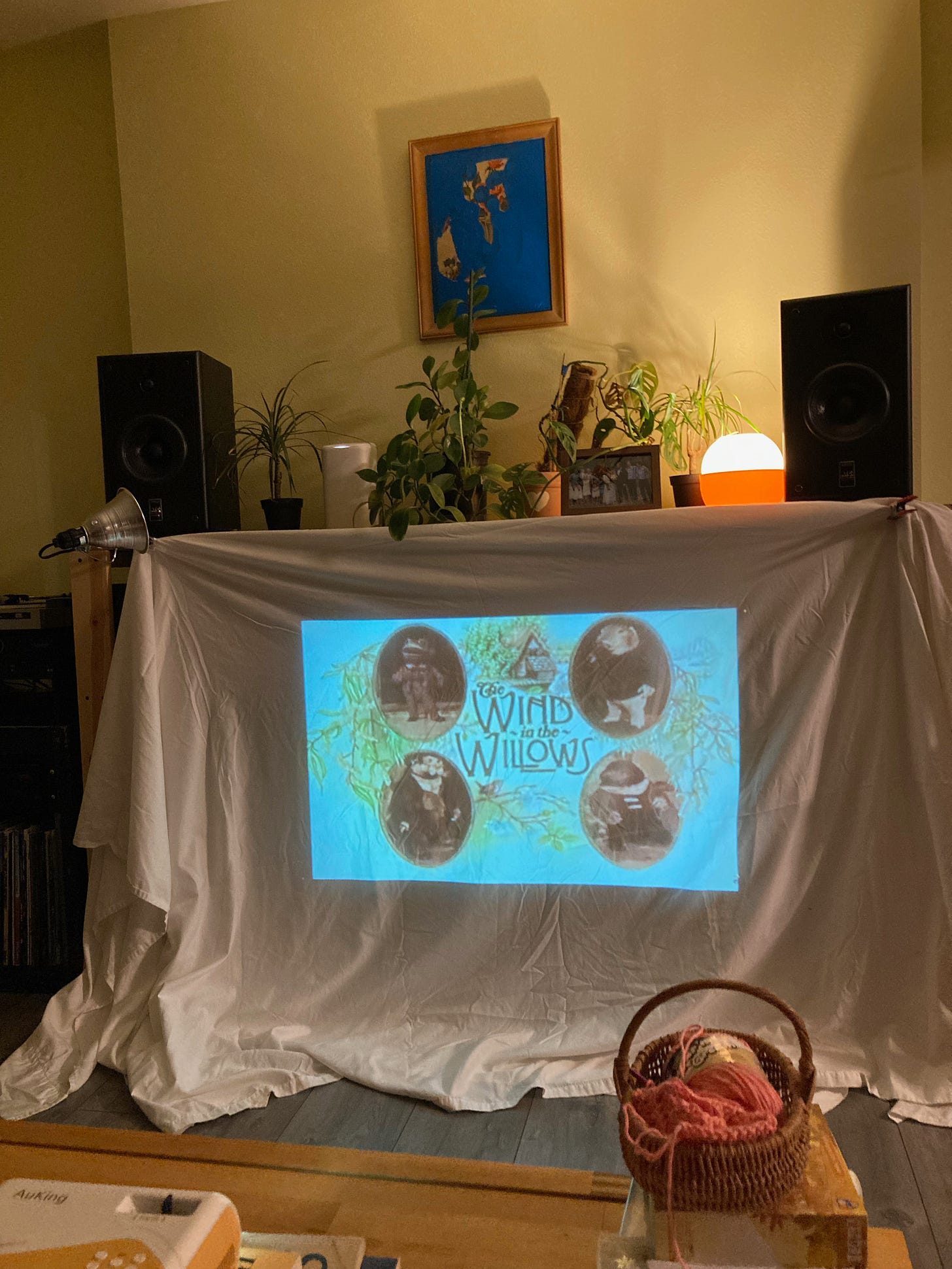 A projector displays "Wind and the Willows" on a sheet in a cozy living room