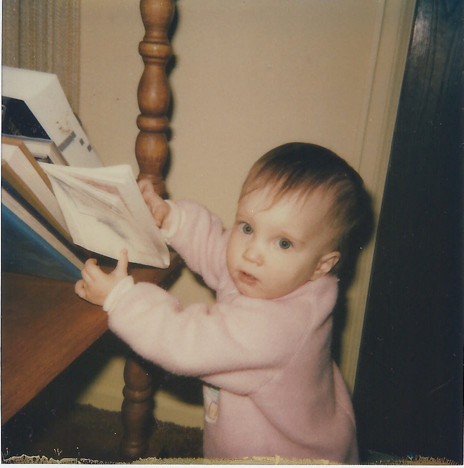 image of the author as a toddler, standing at a bookshelf thumbing through a packet of papers