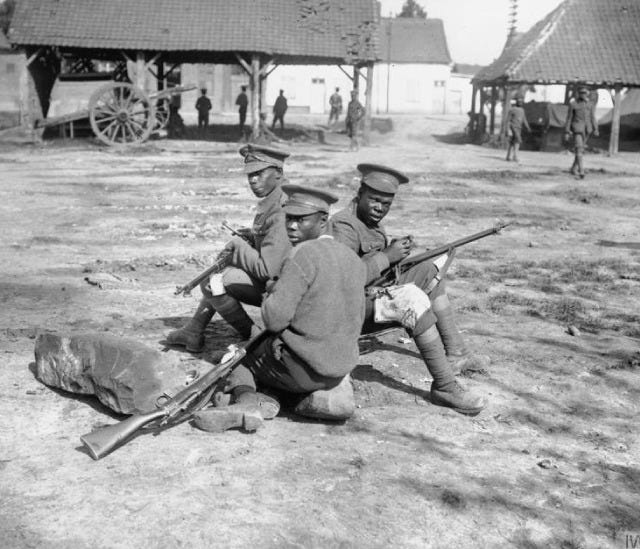 Black and white photo of three young African men who are soldiers in uniform, polishing their rifles during World War I.