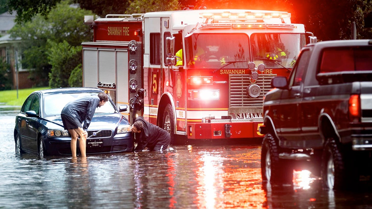 Car stuck in water, firetruck beside, attaching tow hook to car