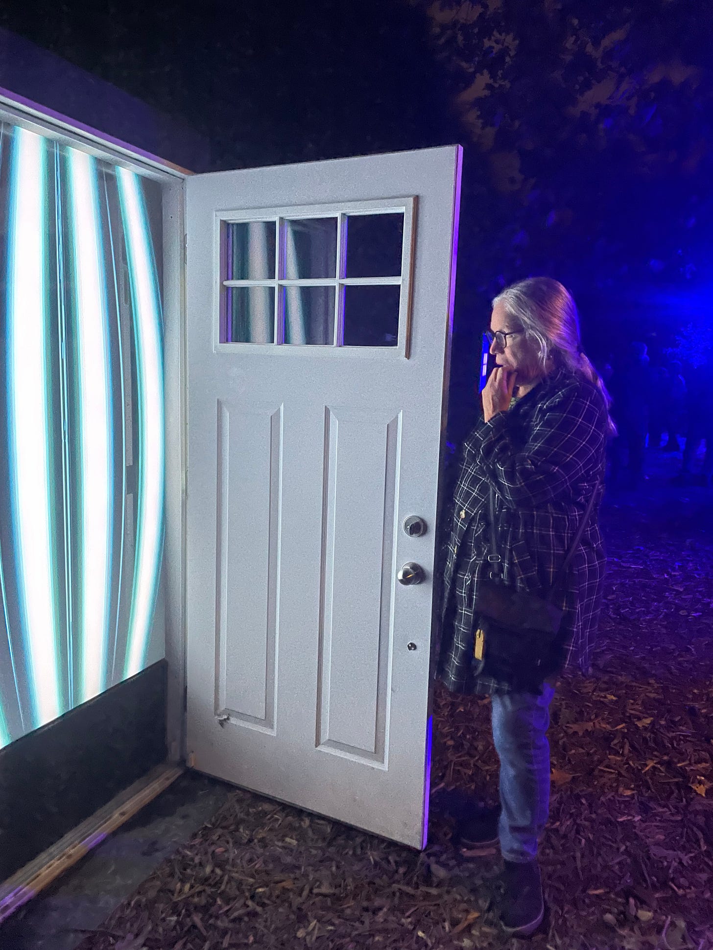 A woman stands at an open door revealing white stripes of light on the other side.