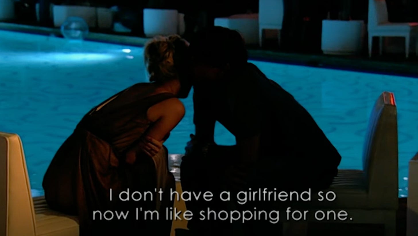 Two people sitting by a lit swimming pool at night, leaning in for conversation. On the bottom of the image, subtitles read: "I don't have a girlfriend so now I'm like shopping for one."