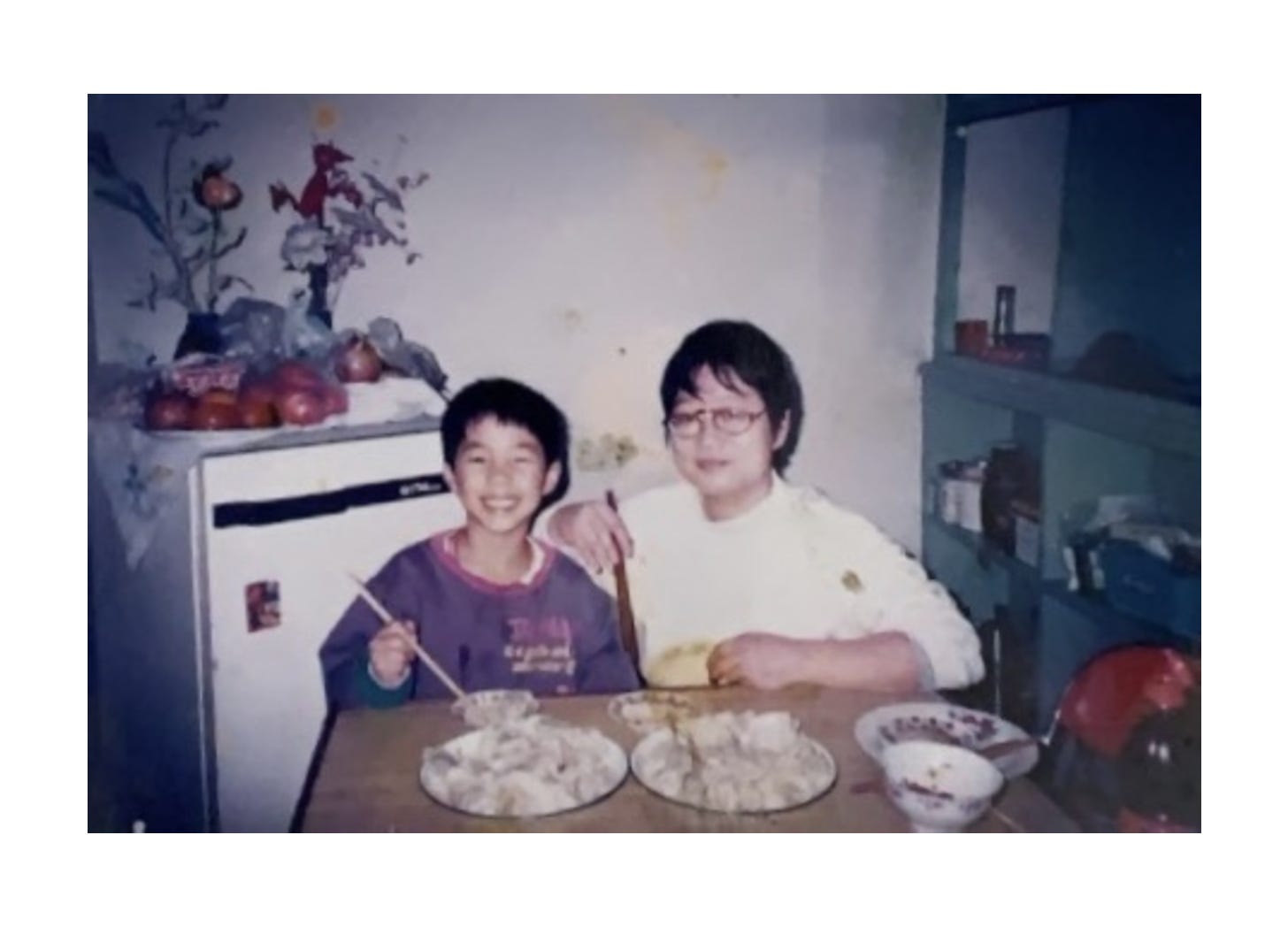 a photograph of myself as a child with my great-aunt in Beijing, seated at her kitchen table with freshly-boiled dumplings a photograph of myself as a child with my great-aunt in Beijing, seated at her kitchen table with freshly-boiled dumplings