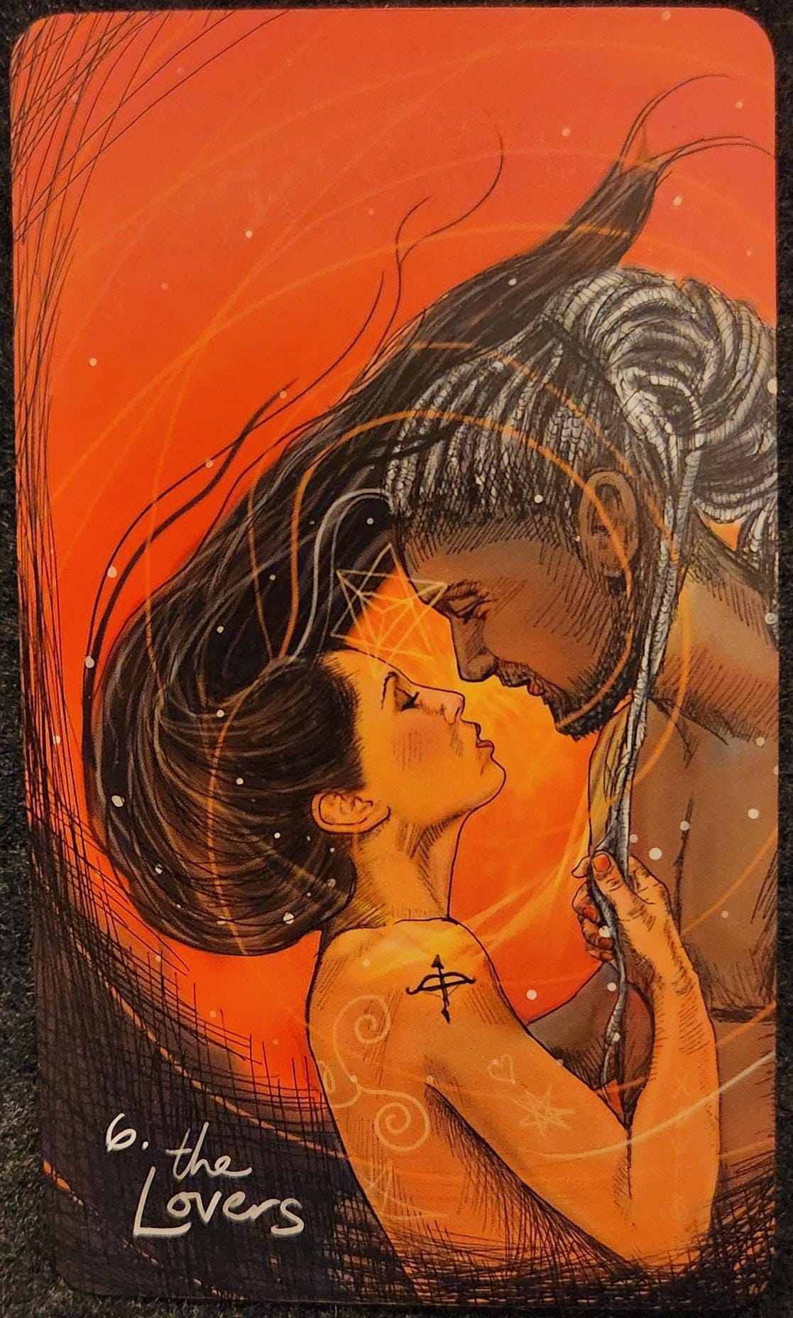 A tarot card labelled 6. The Lovers. A man and woman are standing in an intimate embrace, both apparently naked. Their faces are close together, their eyes are closed. The woman has long brown hair, flowing towards the man. The man has dreadlocks, tied up into a bun. The woman is tugging on a few locks that have come loose. Energy swirls around them. The sky in the background is a bright red. The woman has a tattoo of a bow and arrow on her upper arm. 