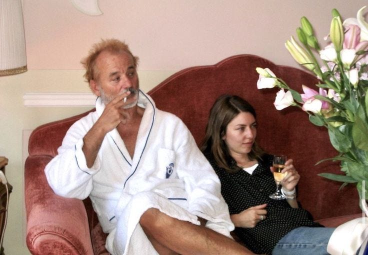 This may contain: an older man and young woman sitting on a couch with wine glasses in their hands