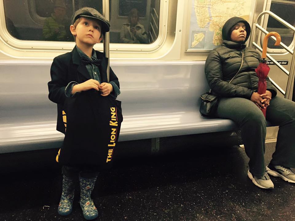 A boy hold a Lion King bag next to a sleeping woman on a New York subway. 