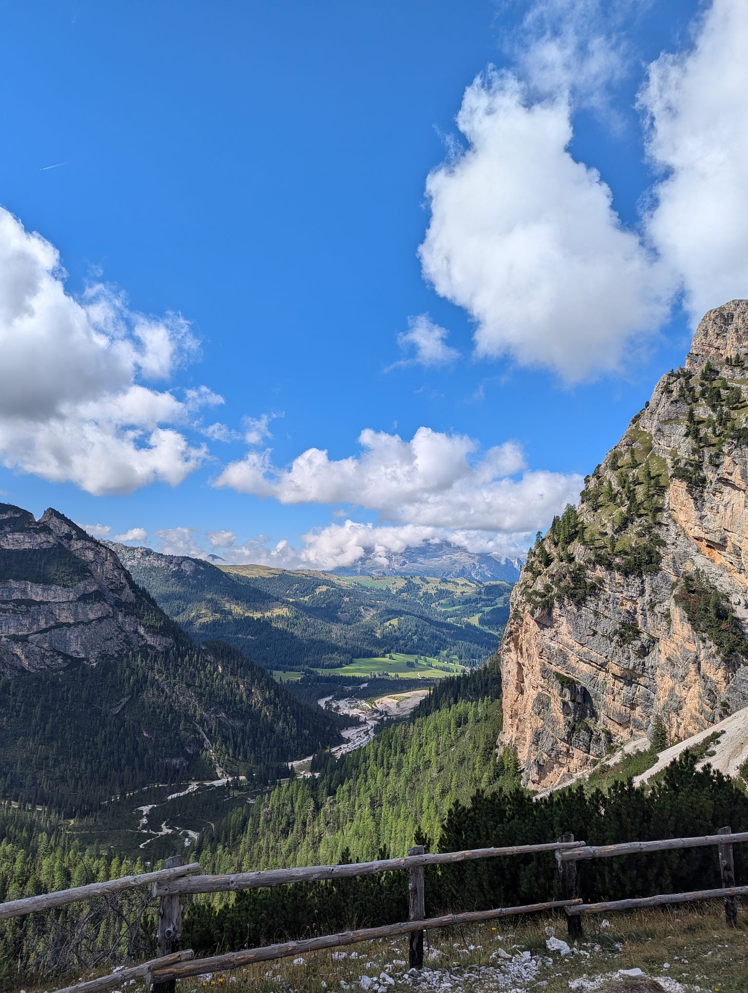 A scenic photo showing a vista in the Dolomites in Italy, flanked by mountains with green meadows in the distance and blue sky above.