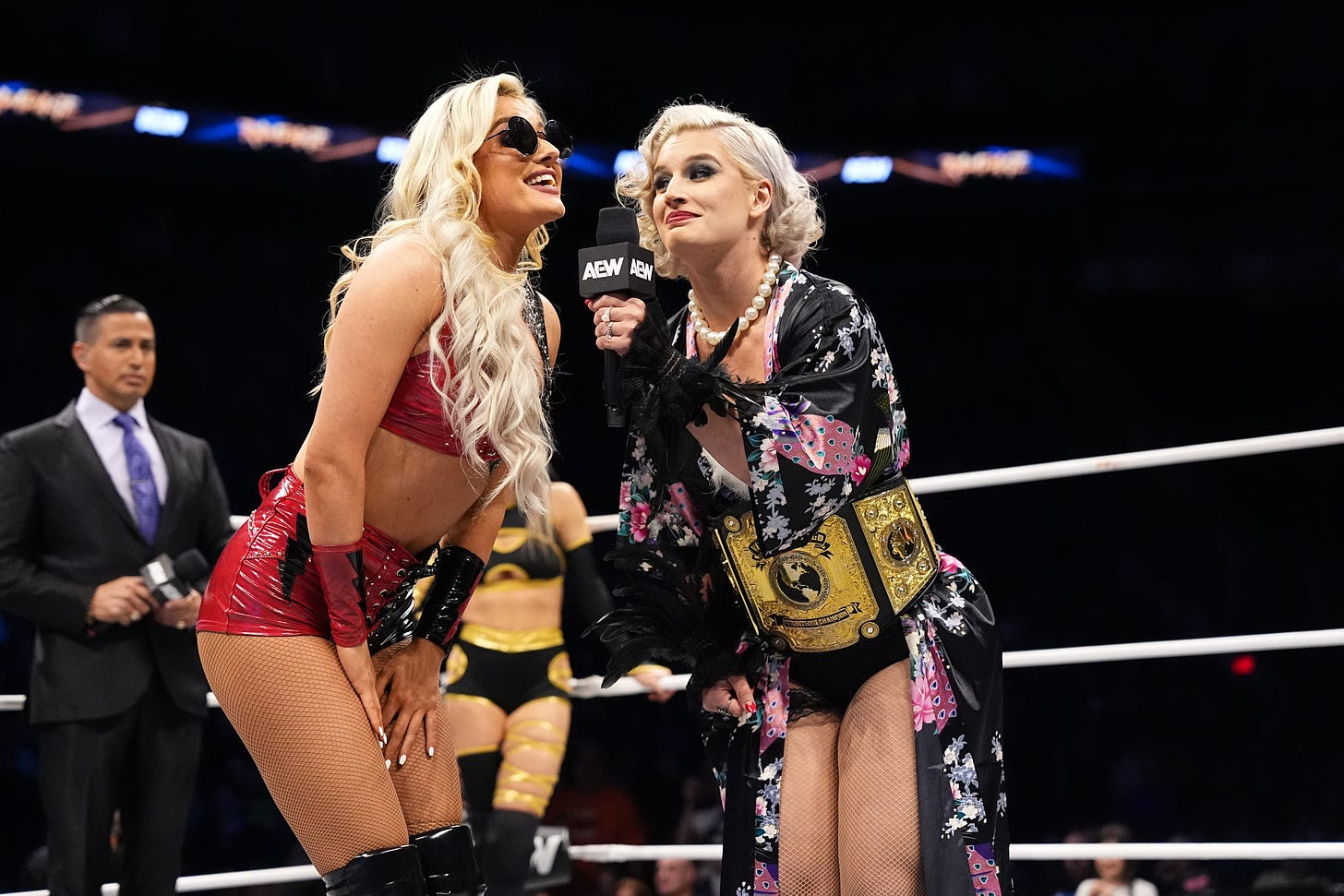 "Timeless" Toni Storm holds up the microphone for Mariah May, clad in her version of Storm's classic gear, to finish her catchphrase; AEW Rampage, March 29, 2024