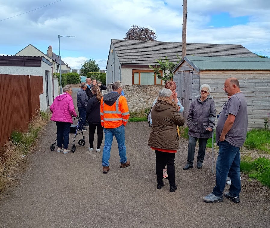 People in discussion outside garages at 'Rate Your Estate'