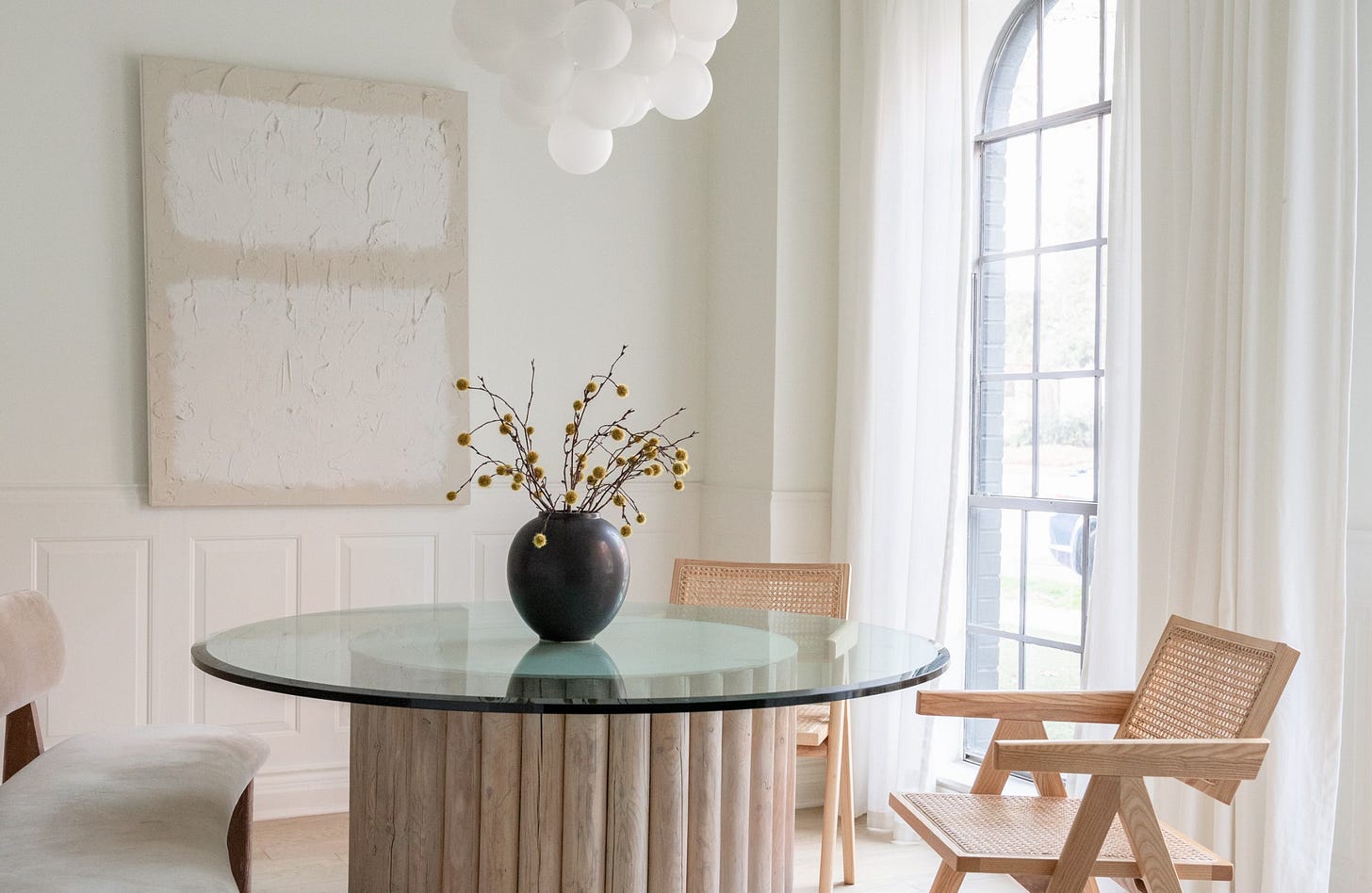 Modern dining room with natural light, a round glass table, wooden chairs, and a vase with branches—evoking calm, clarity, and intentional space. Modern dining room with natural light, a round glass table, wooden chairs, and a vase with branches—evoking calm, clarity, and intentional space.