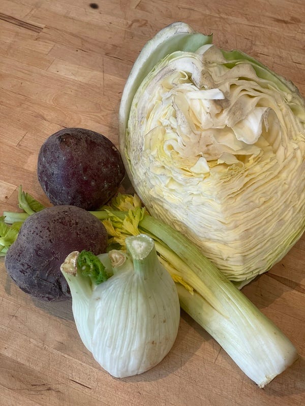 A quarter of a cabbage, 2 beets with light mold on peel, droopy celery, and fading fennel bulb on a cutting board