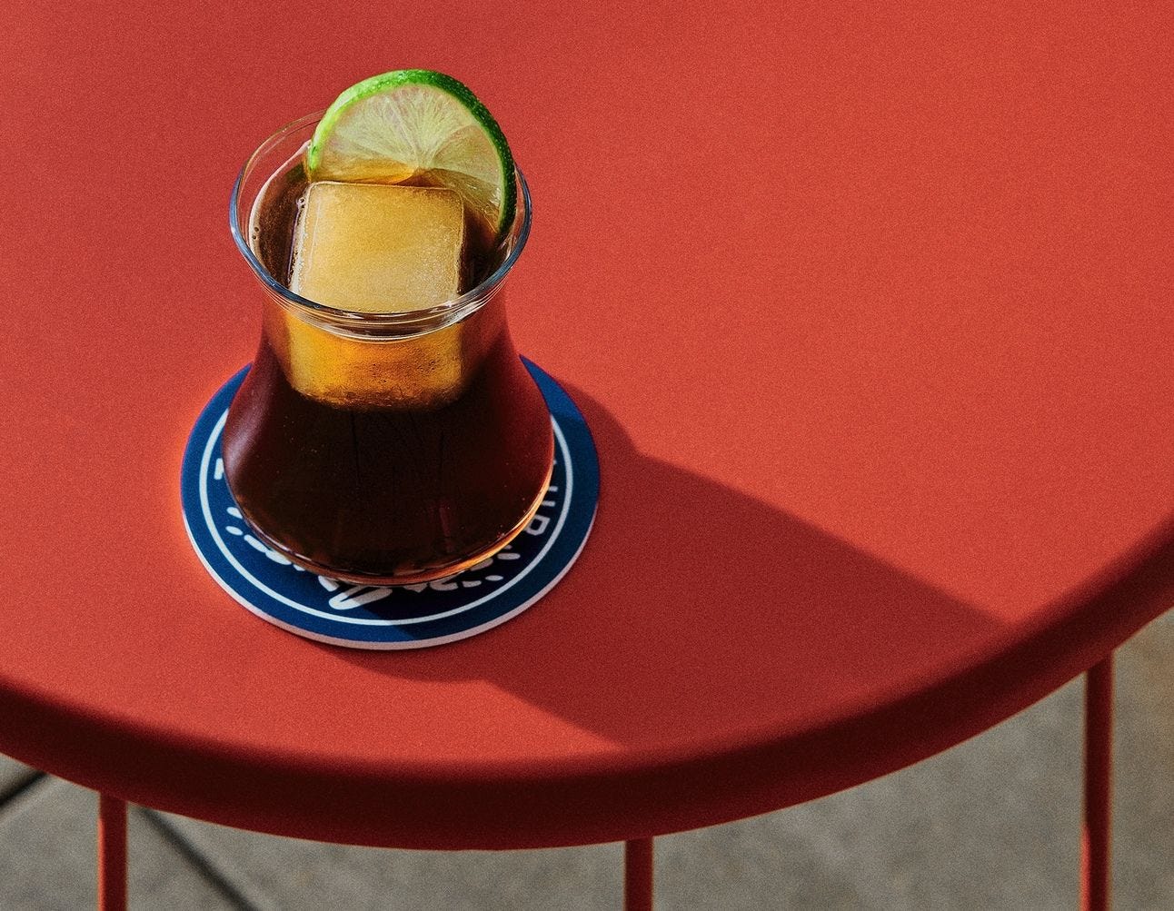 cola cocktail with one square ice cube on a red table