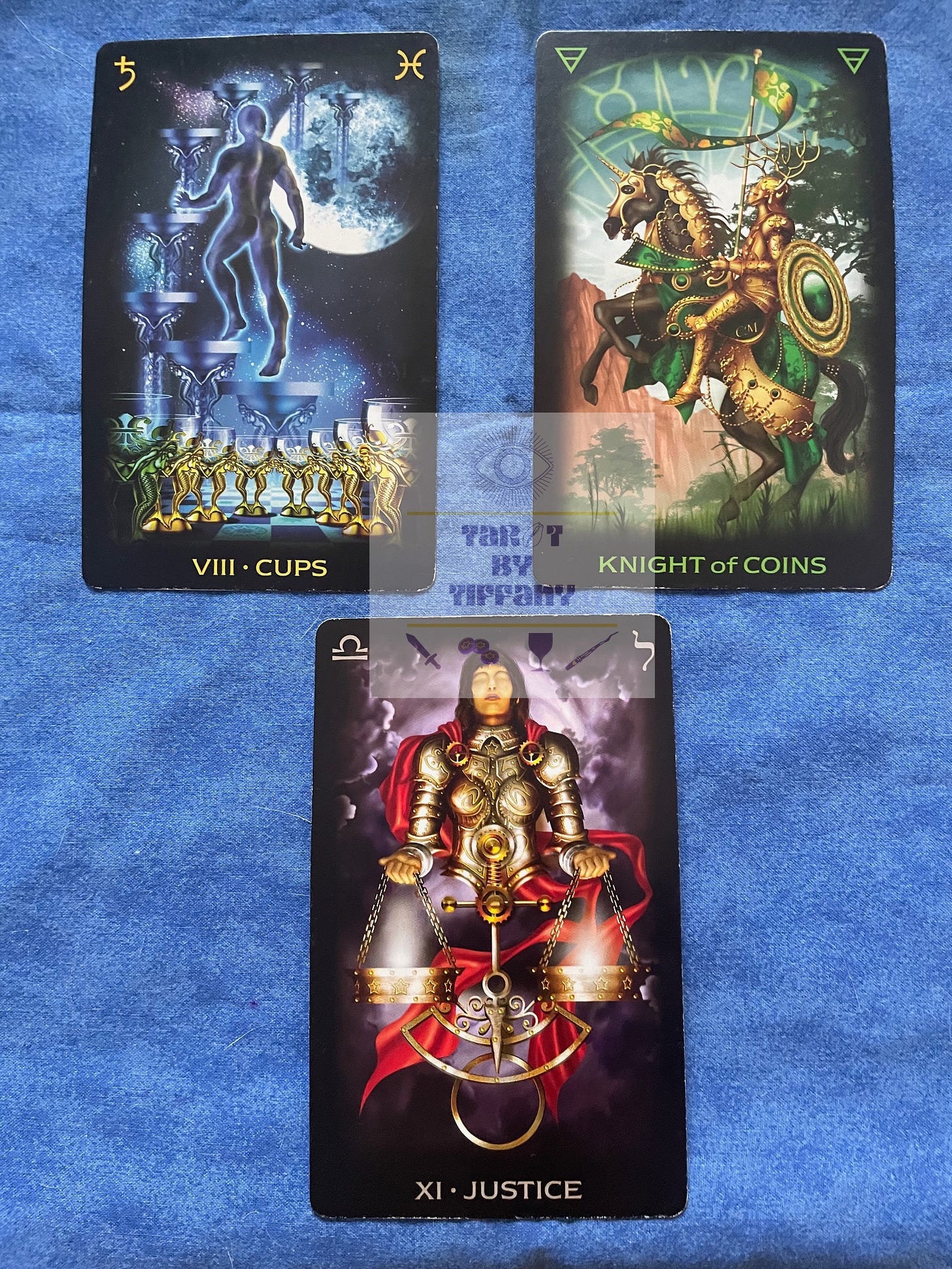 3-card reading with the Tarot of Dreams. Top two cards (L-R): 8 of Cups and Knight of Coins. Bottom card: XI-Justice. The cards are laid out on a cobalt blue cloth background.