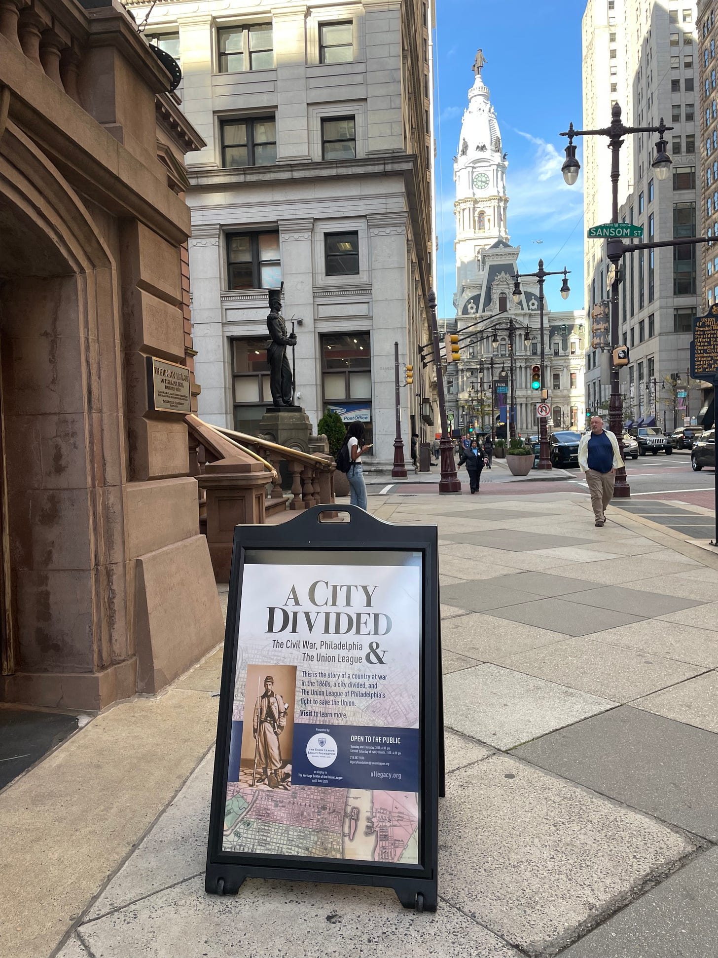 Sidewalk sandwich board exhibit poster on south Broad Street, Philadelphia City Hall in background