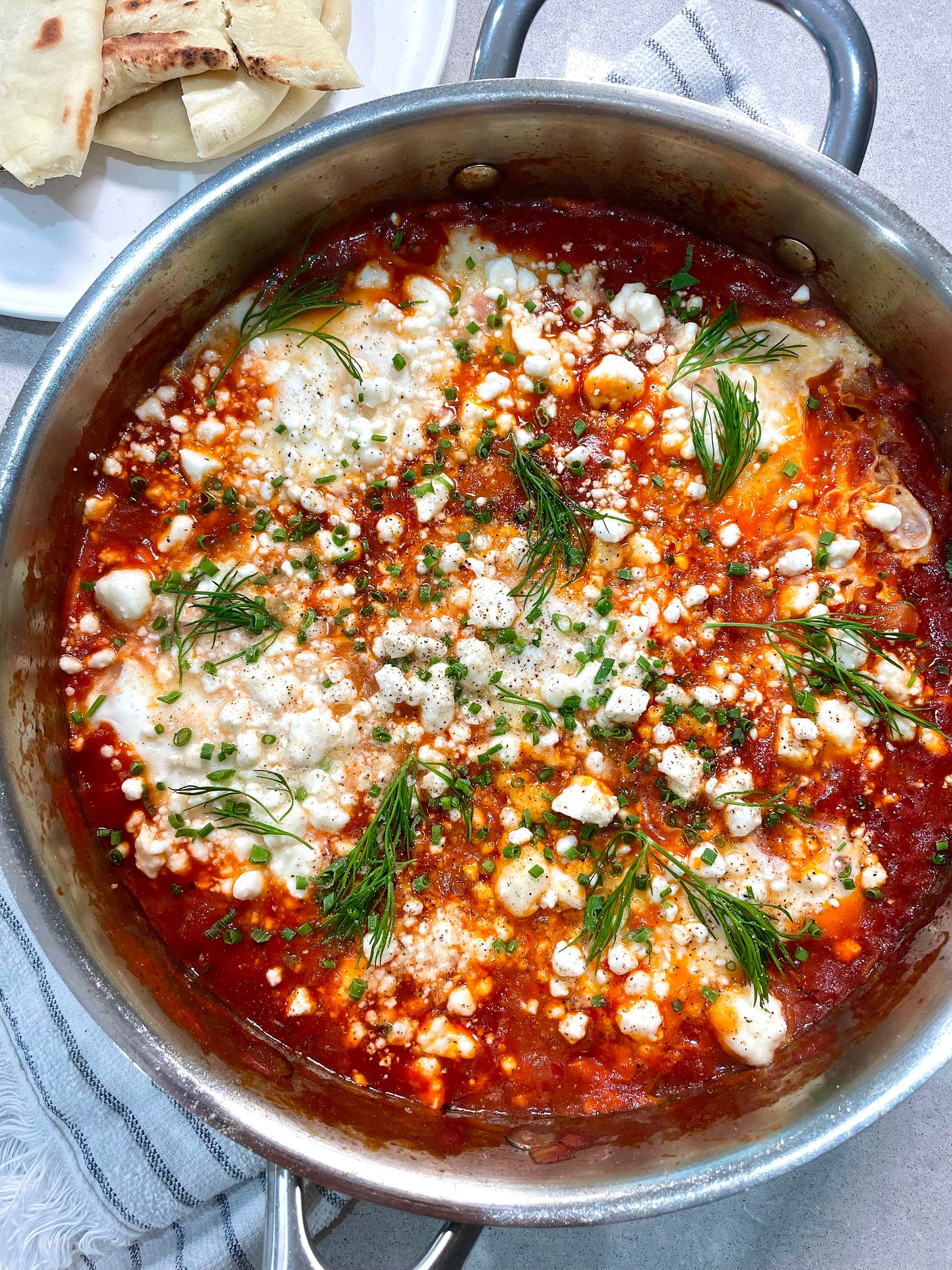 stainless steel pan of cabbage shakshuka with fresh herbs on top