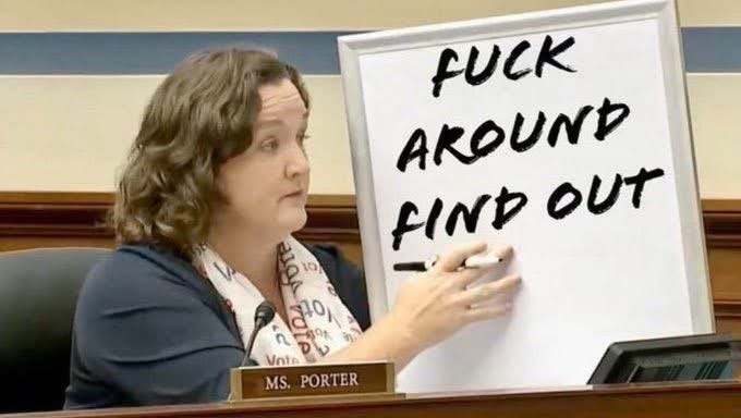 Katie Porter sits, holding her hand on a whiteboard. On it is written "fuck around find out" in black marker.