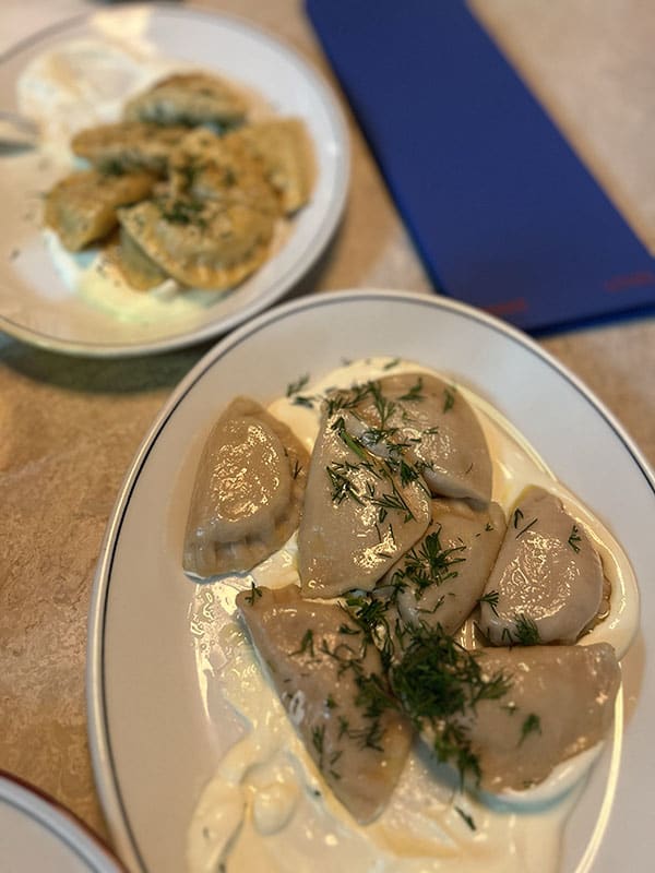 Two plates of pierogi, with dollops of sour cream.