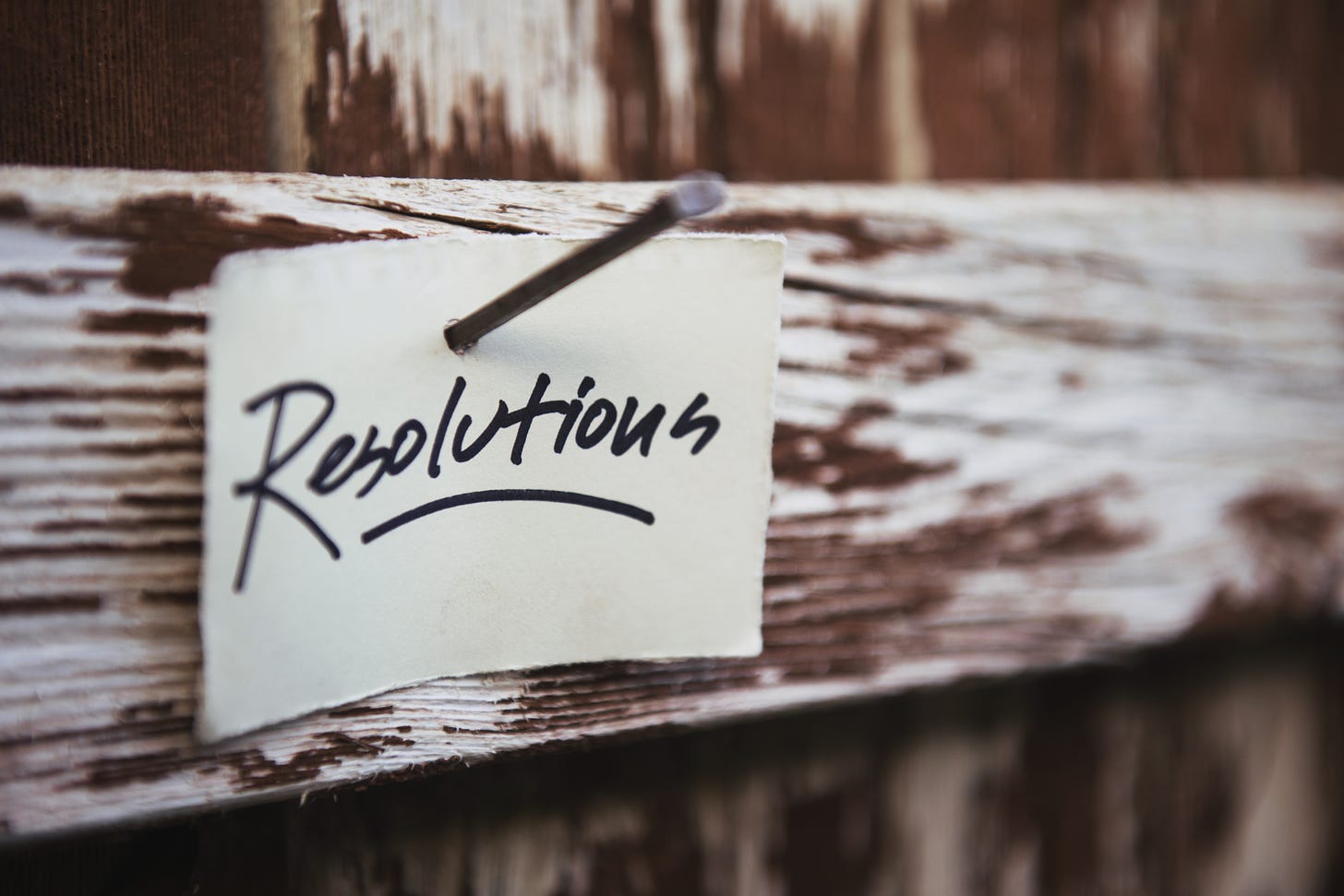 The word "resolution" is written in black ink on a white index card. The card is nailed to a wooden beam.