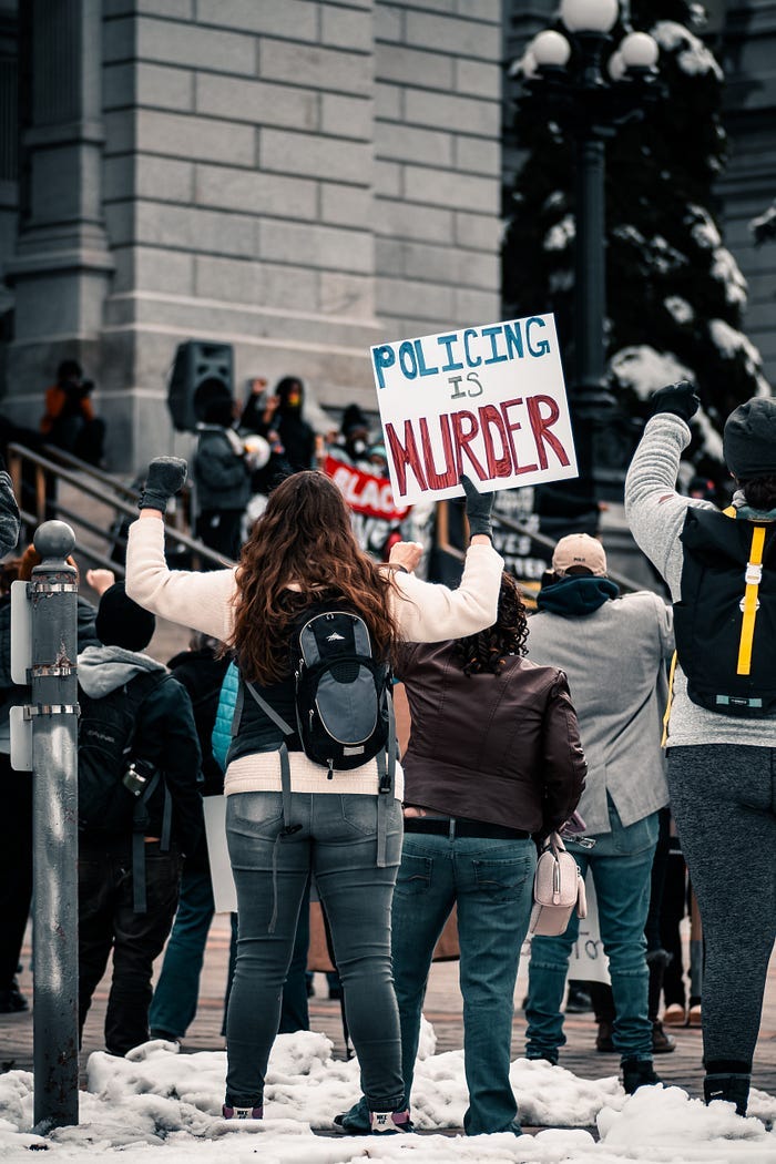 A Black Lives Matter protestor holds up a sign that reads: Policing is Murder. A Black Lives Matter protestor holds up a sign that reads: Policing is Murder.
