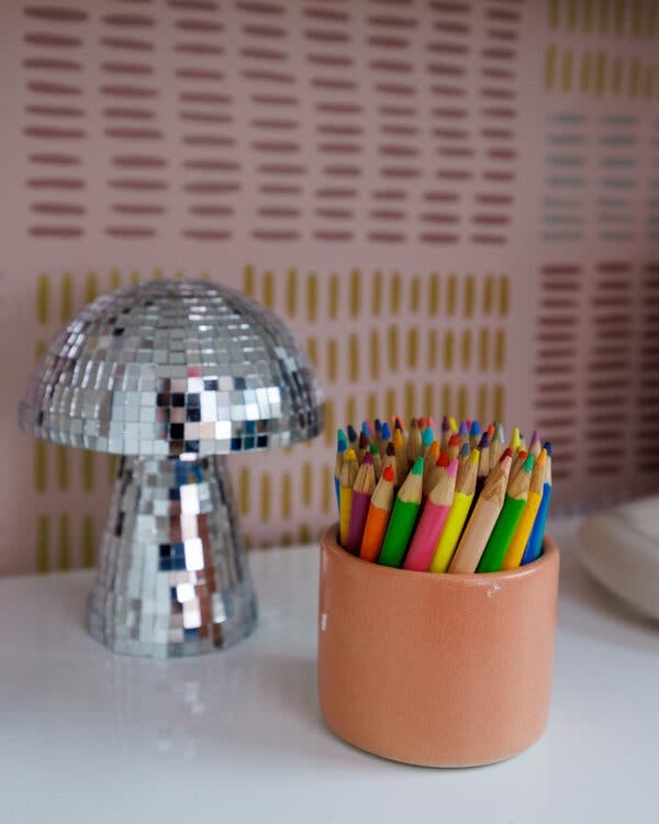 A close-up of a ceramic container holding colored pencils next to a mirrored mushroom light.