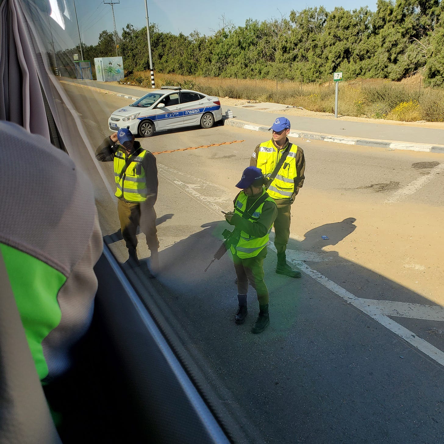 Three IDF soldiers in yellow bests and carrying assault rifles stand outside our bus.