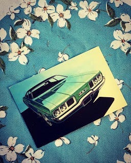 A postcard of an old green car sits on a turquoise and white tablecloth