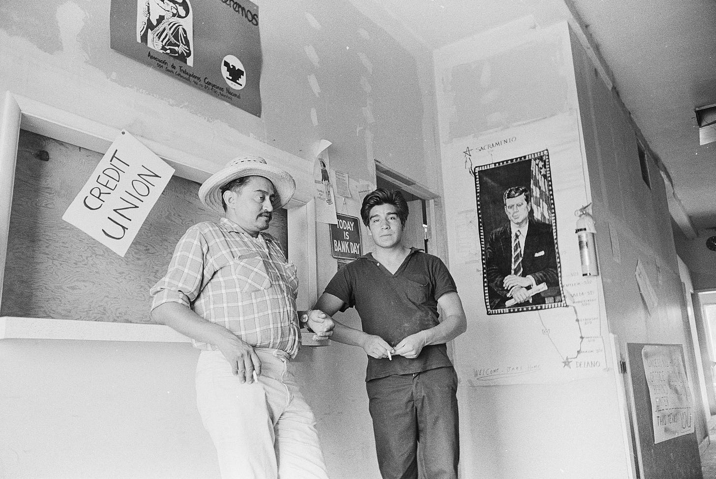 Tony Orendain (left) and a farm worker stand in front of the National Farm Workers Association credit union at Forty Acres in Delano, California. Photo by John Kouns © Tom and Ethel Bradley Center