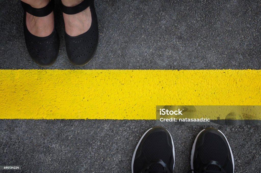 Legs of a couple standing opposite each other Legs of a couple standing opposite each other divided by the yellow asphalt line top view Boundary Stock Photo