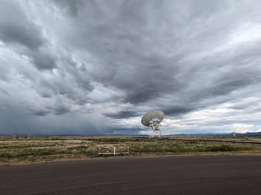 picture of a radio antenna at the VLA. the antenna is small compared to the vast sky and field above and below it.