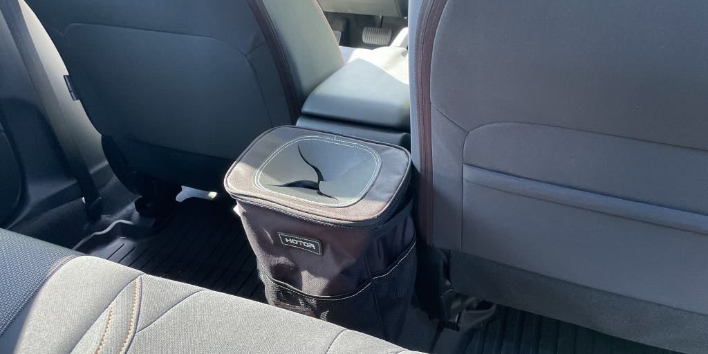 The HOTOR car trash can attached to the rear of the middle console of a car.