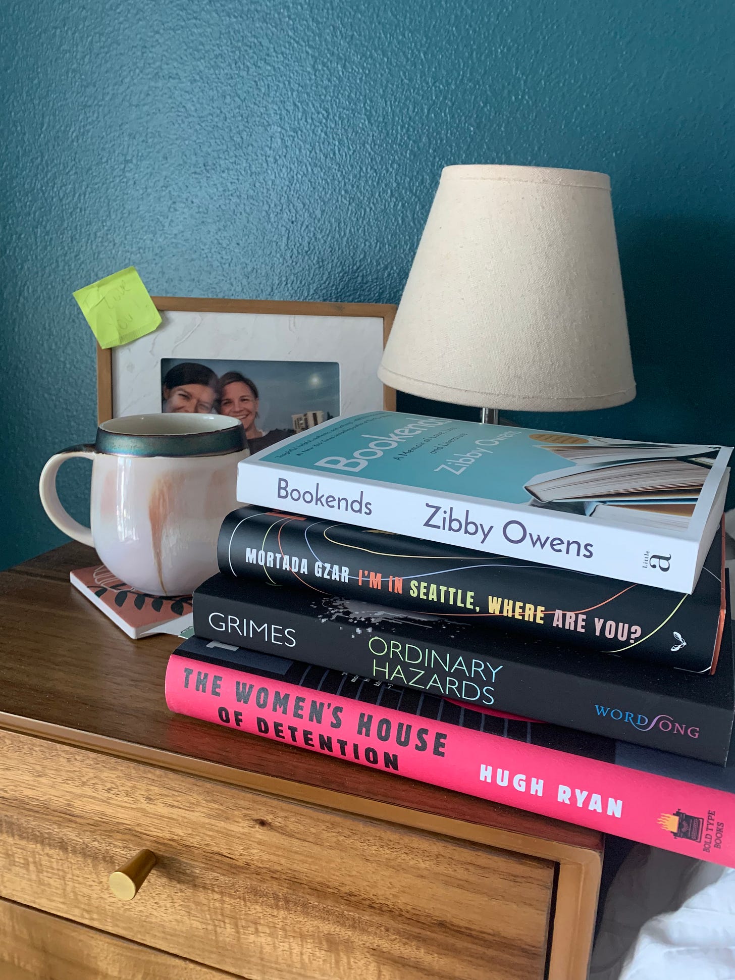 Beige and brown coffee mug sits next to a stack of books from queer, black, and Jewish authors.