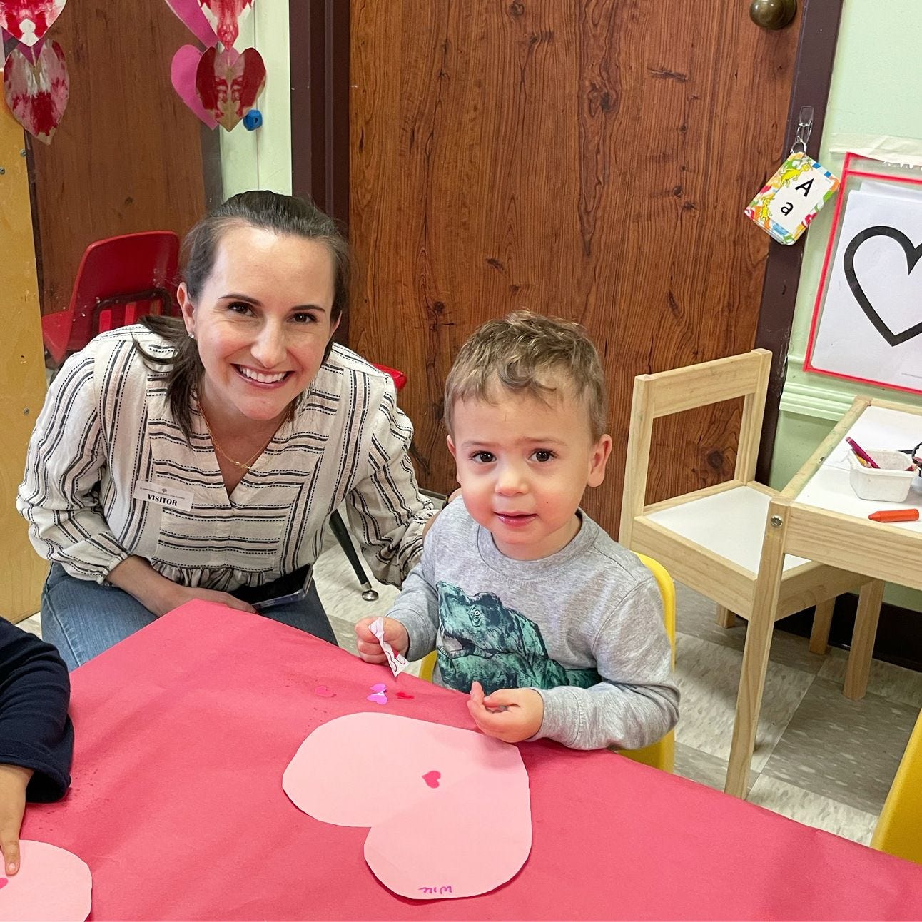 A mom and son smiling while doing a valentines day craft at school.